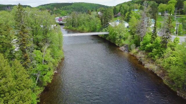 Survol en drone de la  rivi&egrave;re &agrave; saumon Matap&eacute;dia. Passage sous la passerelle du site Patrimonial de p&ecirc;che Matamajaw jusqu'a l'embouchure de la rivi&egrave;re Causapscal. P&ecirc;cheur et clocher en arri&egrave;re-plan.