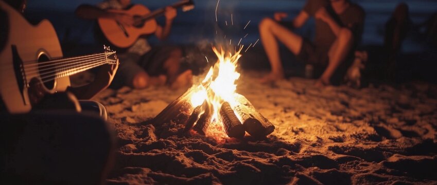 Blurred group of young people having fun sitting near bonfire on a beach at night playing guitar singing songs