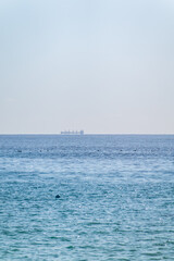 Calm blue sea with the silhouette of a large ship on the horizon