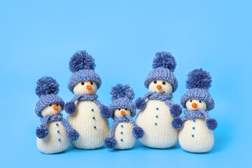 Family of knitted snowmen celebrate the holidays on blue background. Winter fairy tale story with your own hands, hobby. Merry Christmas and New Year 2025 greeting card