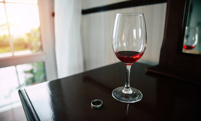 Close up image of glass of wine with marriage ring on the table. Result of betrayed. Divorce concept