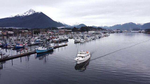 Aerial view of boat leaving harbour Sitka, Alaska, late winter snowcapped mountains and cold ocean. Cinematic drone video
