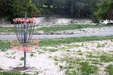 Disc Golf Basket With Chains on Sandy Grass With a River and Trail in the Background