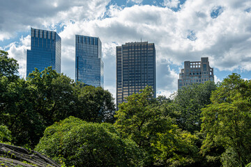 Obraz premium New York, NY, USA - August 2, 2023: Highrise buildings on SW side of central park under blue cloudscape. Green foliage in front