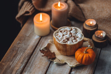 Spicy sweet fall hot drink: delicious pumpkin latte with cinnamon, marshmallow with salted caramel. Served in handmade artisan mug in shape of pumpkins, cozy home decor with candles, dry autumn leaves