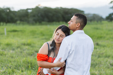 young latin couple, very loving caucasian woman hugging her boyfriend's hand while leaning on his shoulder with closed eyes