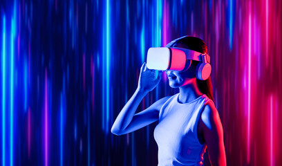 Smart female standing surrounded by neon light wearing VR headset connecting metaverse, future cyberspace community technology. Elegant woman looking faraway and smiling satisfactorily. Hallucination.