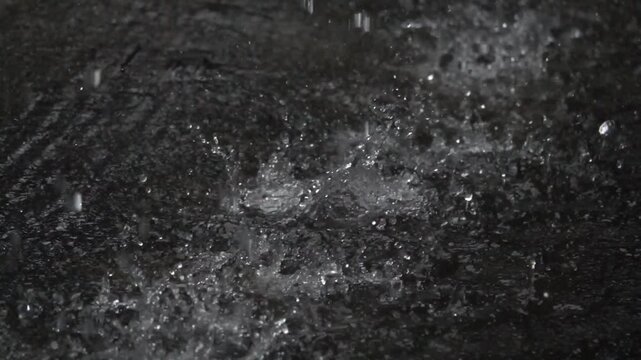 A black and white photo of rain falling on a dark surface. Scene is somber and melancholic, as the rain seems to be falling heavily and the surface appears to be desolate