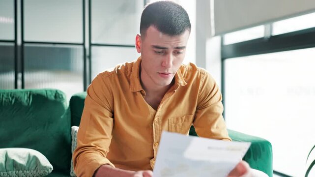 Man, stress and reading documents in home for financial crisis, bankruptcy and mortgage loan debt on sofa. Male person, anxiety and paperwork in house for medical results, bills and eviction letter