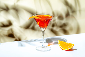 Orange cocktail with red vermouth, liqueur, bitter, citrus zest and ice in martini glass on beige...