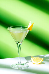 Alcoholic cocktail drink with gin, vodka, aperitif, lemon zest and ice in glass on green background, hard light