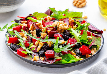 Fresh crispy vegan salad with baked beetroot, dried prunes, arugula, chard and lnuts, white background