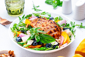 Gourmet summer fresh salad with peaches, chicken, blueberries, onion, feta cheese, basil and arugula, white background, top view