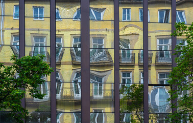 A distorted facade of a yellow building reflecting of a mirrored glass building