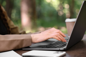 Businesswoman working with laptop at wooden table outdoors, closeup. Remote job