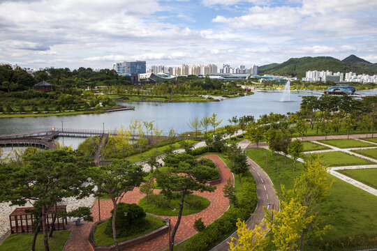 Sejong-si, Chungcheongnam-do, South Korea - September 2, 2022: High angle and summer view of trees and trail against Sejong Lake and apartments at Sejong Lake Park
