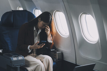 Photo of a frustrated woman sitting on an airplane with her head in her hands. Asian woman sitting...