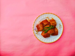 Boiled Cassava with Palm Sugar, is a traditional Indonesian dessert made from boiled cassava, combining the sweetness of brown sugar and the soft texture of cassava. Served on a pink background.