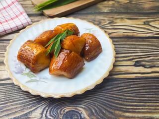 Boiled Cassava with Palm Sugar, is a traditional Indonesian dessert made from boiled cassava, combining the sweetness of palm sugar and the soft texture of cassava. Served on a wooden table.