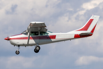 Unmarked and generic high wing general aviation aircraft.  Red stripe on white paint of a piston powered propeller driven airplane on approach to landing