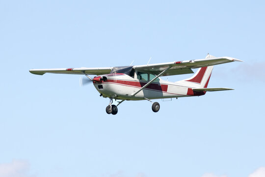 Light general aviation aircraft on appraoch to landing. Red and white classic high wing airplane and spinning propeller. Isolated on plain background - Powered by Adobe