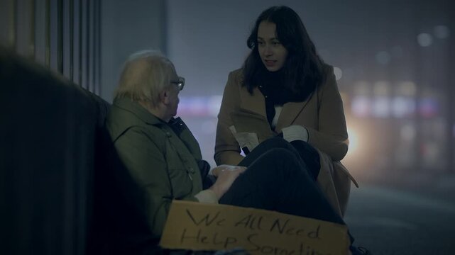 A compassionate woman helping a homeless man in the city at night in the cold and darkness
