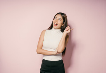 Cheerful Young Woman Pointing Upwards Against Pink Background in Studio Setting