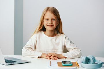 Naklejka premium Smiling girl using laptop for elearning at home A cute teenage girl is happily sitting at her desk, surrounded by books and notebooks With a big smile on her face, she wears headphones while typing on