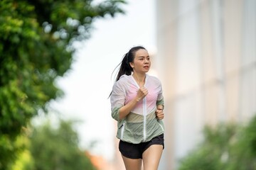 A woman is running in a park with a green jacket and black shorts