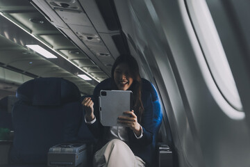 Young Asian executive excels in first class, multitasking with digital tablet, laptop and...