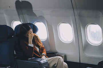 Photo of a frustrated woman sitting on an airplane with her head in her hands. Asian woman sitting...