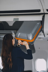 Female tourist packing her luggage in the airplane cabin.