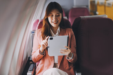Attractive Asian female passenger of airplane sitting in comfortable seat while working laptop and...