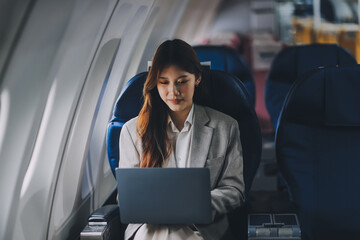 Joyful asian woman sits in the airplane and using tablet while go to travel