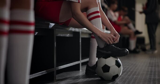 Girl, hands and tying shoes with soccer ball in locker room for preparation, getting ready or match. Closeup of female person, sports athlete or tie laces for practice tournament or football training