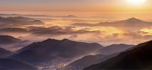 High angle and panoramic view of sea of clouds on the city and mountains at sunrise seen from Ganwolsan Mountain near Ulju-gun, Ulsan, South Korea  © JinChang