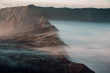 In the early morning, clouds drape gently over the village nestled beneath the volcano.