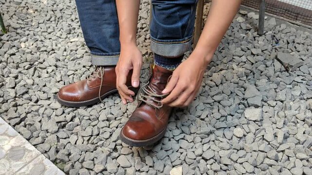 Man in jeans putting on and tying red leather boots shoes, in rock floor, rugged, stock video, 4K.