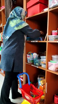 A female therapist wearing a hijab holds a lesson plan and selects toys to use during a therapy session with children.