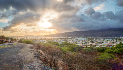 Hawaiian asphalt road trip with a view to a small village during sunset phase with rain clouds at the background