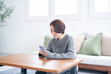 リビングで携帯を持ち笑うショートヘアー女性