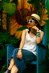 Woman wearing a hat, white sunglasses, and a white blouse sitting in a blue armchair