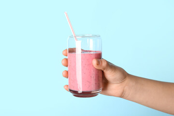 Female hand with glass of pink smoothie on blue background
