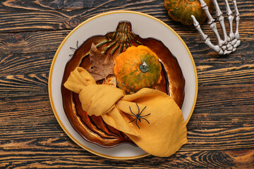 Festive table setting with Halloween pumpkins, spiders and skeleton hand on brown wooden background