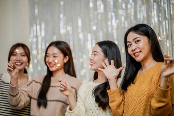 Cheerful friends enjoying home Birthday holiday party. Asian Friends hold lights with sparkling Sparkler celebrating Christmas or New Year eve party.