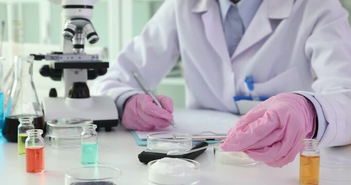 Scientist transfers powder into container to measure weight. Professional researcher records exact weight of powder in lab notebook