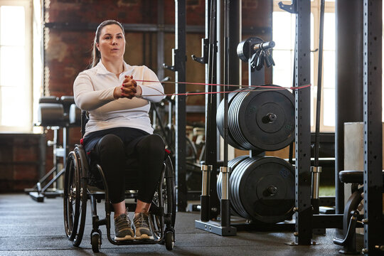 Full length portrait of adult woman with disability training with elastic bands in gym copy space
