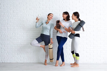 Sporty young women with yoga mats and water bottles near white brick wall © Pixel-Shot