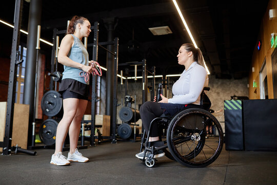 Full length side view of female fitness trainer assisting woman with disability during training in gym copy space