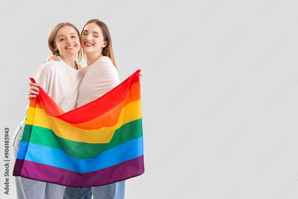 Wall mural Young lesbian couple with LGBT flag on light background